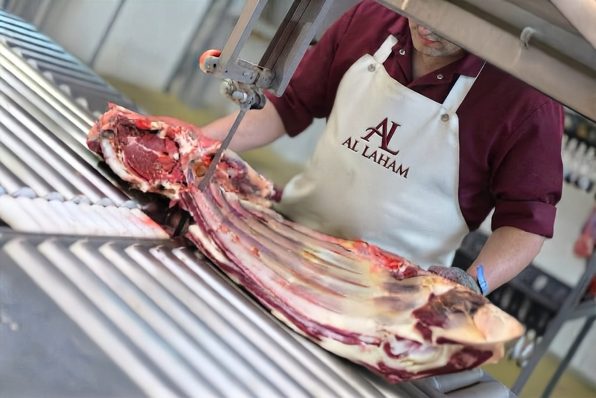 Butcher in an Al Laham apron cutting a beef rib section on a band saw