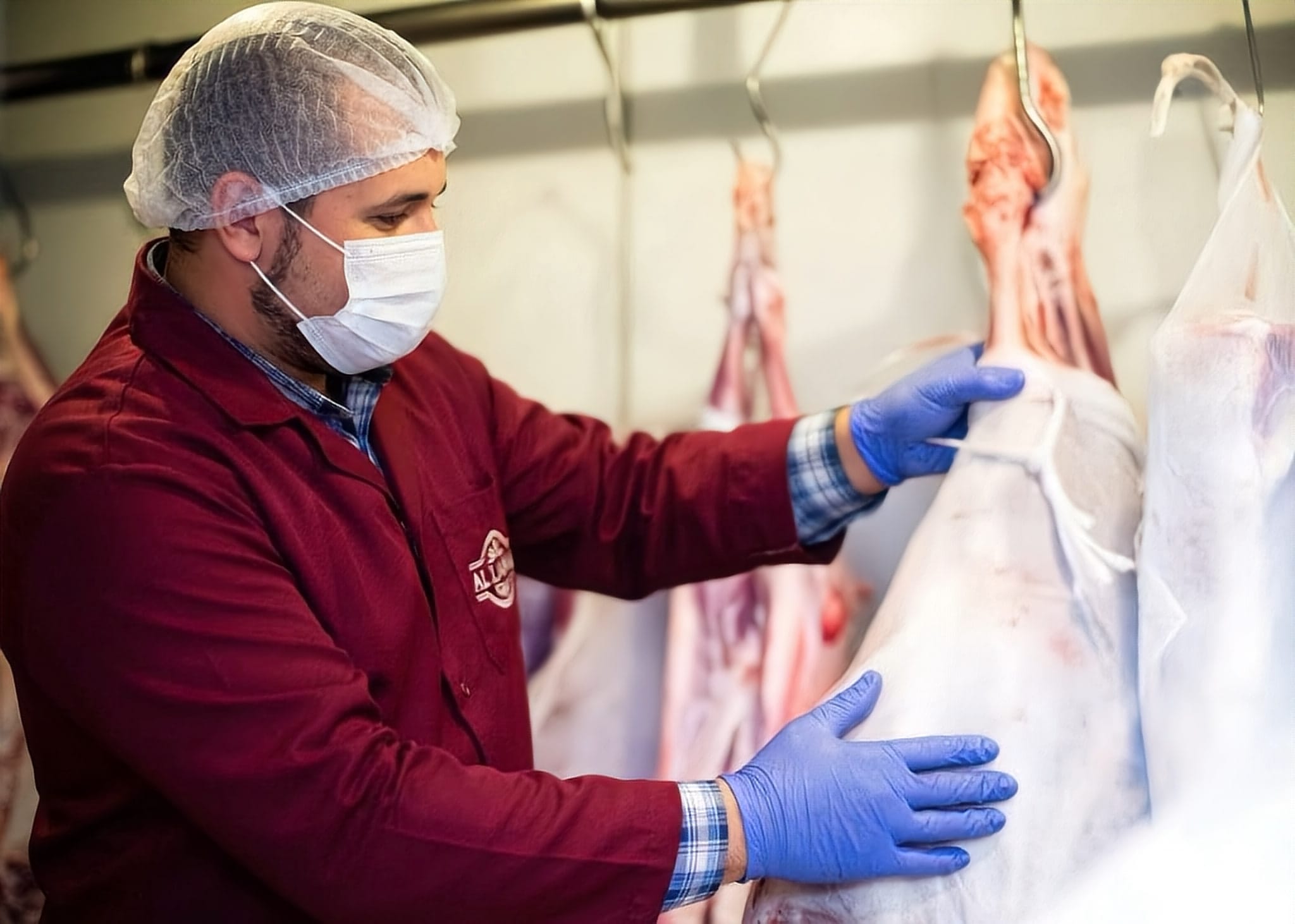 Worker in hairnet, mask and gloves handling a wrapped carcass on the rail