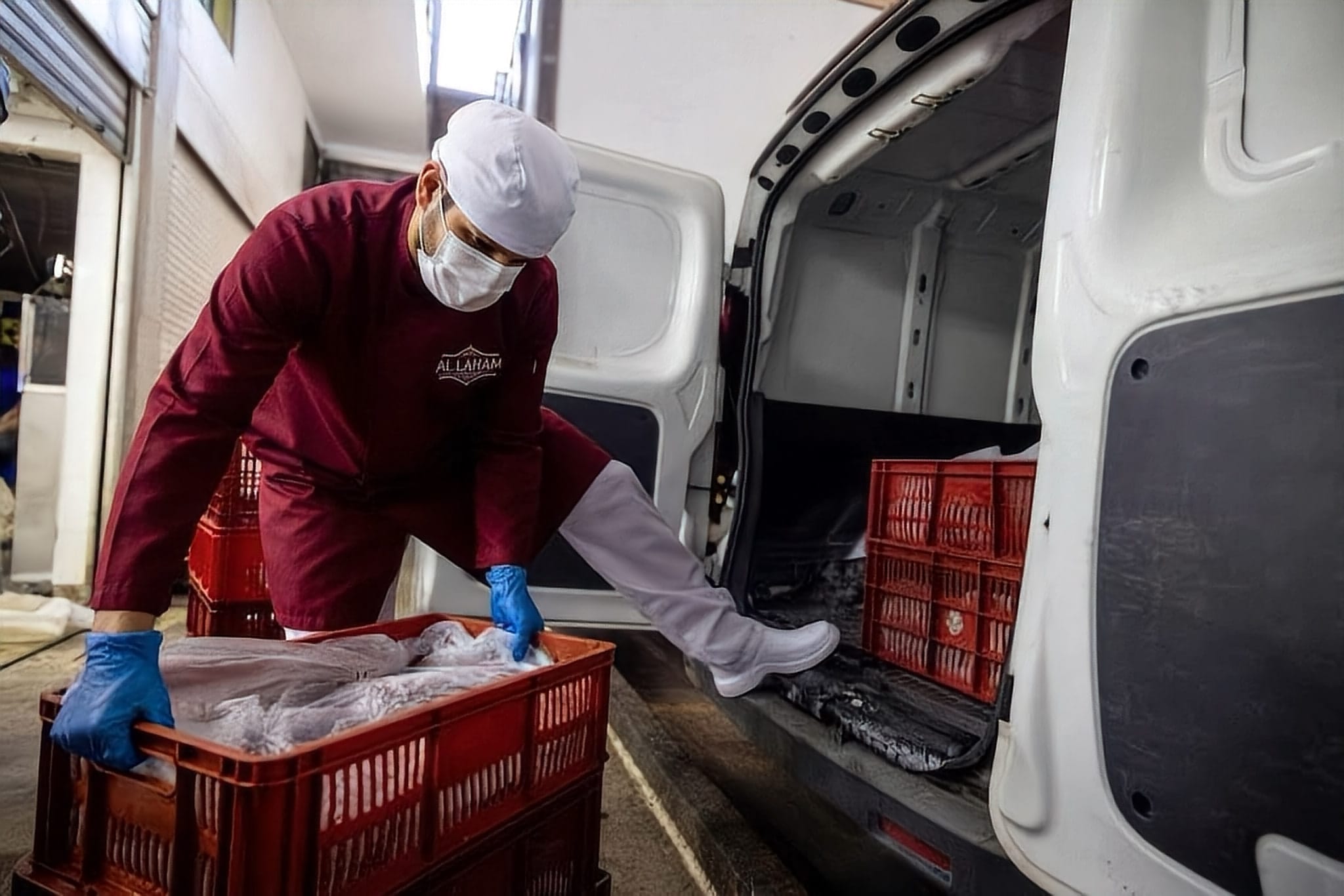 Worker in uniform, mask and gloves loading crates into a refrigerated van